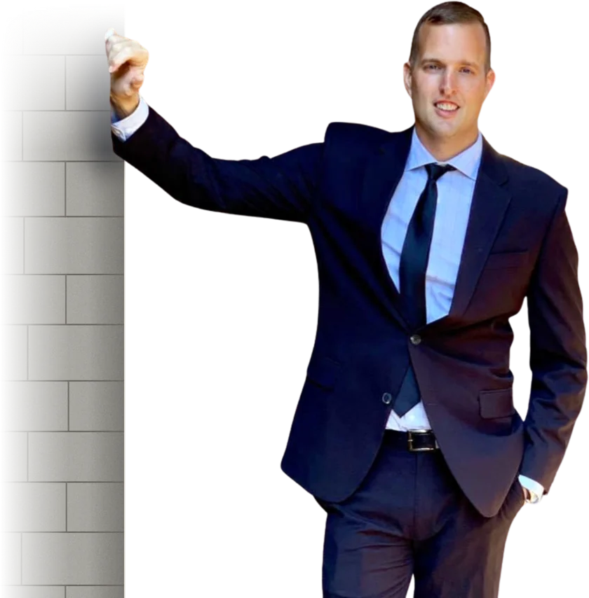 Jason Moore in a navy suit, leaning on a stone wall and smiling